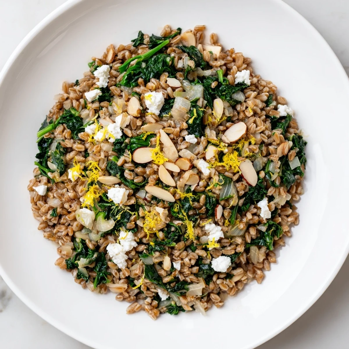 Close-up of a steaming bowl of Warm Farro & Greens Pilaf sprinkled with toasted almonds and feta.