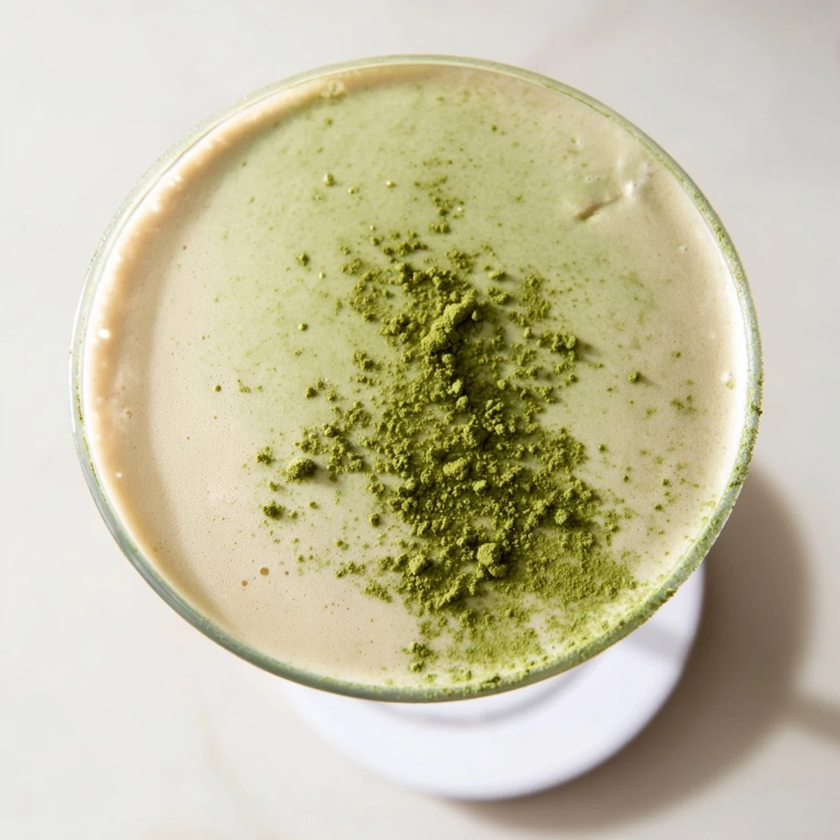 This creamy Matcha Martini features frothy pale green liquid in a martini glass, with matcha powder dusting on top.  