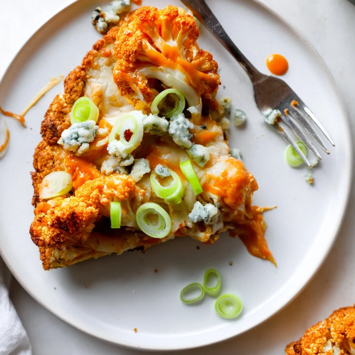 A close-up of Buffalo Cauliflower Pizza with melted cheese and fresh green onions on a rustic wooden table.  