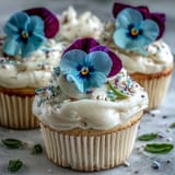 Baby in Bloom Cupcakes with edible flower toppers on a white plate, soft vanilla buttercream swirls and colorful edible flowers create a springtime dessert centerpiece.