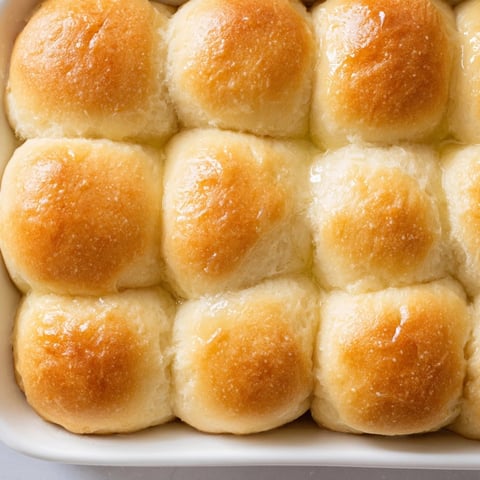 Golden brown Fluffy Buttermilk Dinner Rolls, fresh from oven, glistening with melted butter.
