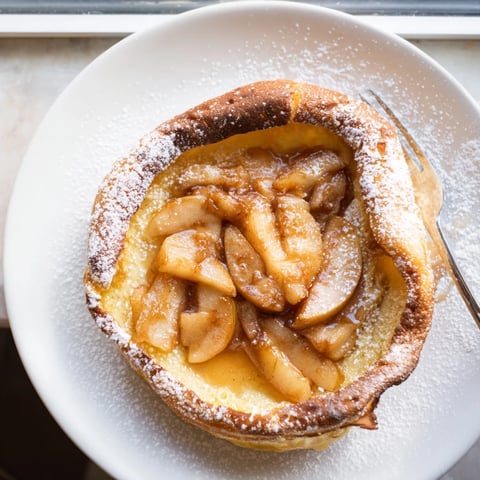 Fluffy Warm Apple Cinnamon Dutch Baby topped with powdered sugar, perfect for brunch gatherings.  