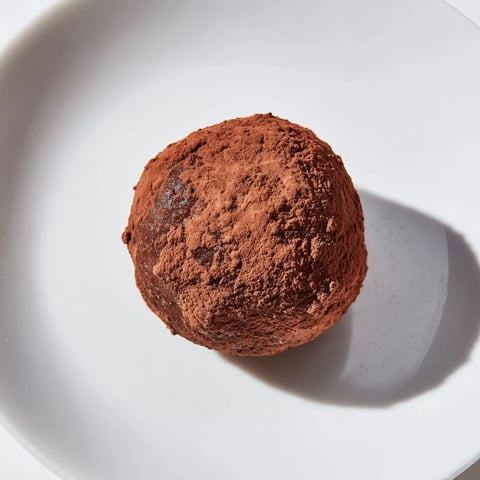 Close-up shot shows rich Date & Walnut Truffles, perfectly round, coated in dark cocoa powder.