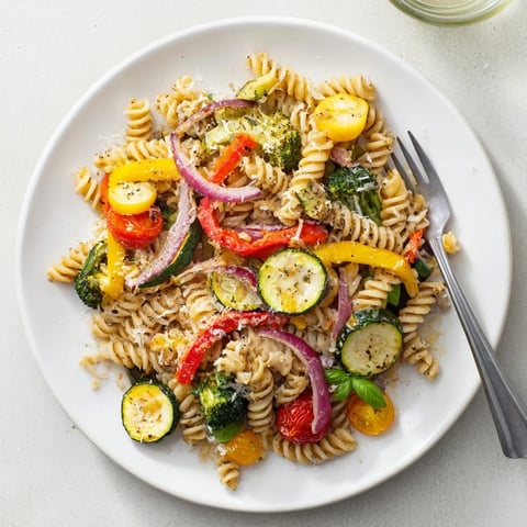 A close-up of pasta primavera in a white bowl, showcasing roasted zucchini, bell peppers, and cherry tomatoes tossed with penne.  