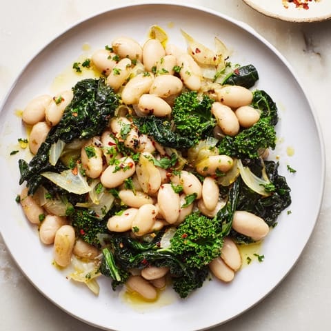 A rustic bowl of Garlicky Beans with Winter Greens, lemon is drizzled, ready for a comforting bite.