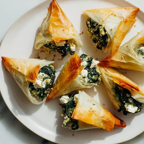 Golden, flaky mini Spanakopita triangle cluster, a delicious Greek appetizer ready to enjoy.