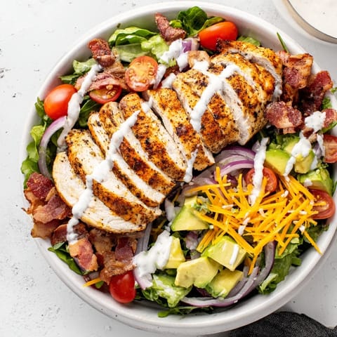 A close-up of a flavorful Crispy Bacon Chicken Salad, showing bacon bits and colorful tomatoes.