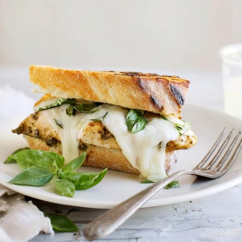 Ciabatta roll halves filled with juicy grilled chicken, melted mozzarella, and vibrant pesto, capturing a golden, crunchy texture for a hearty Italian-American sandwich.