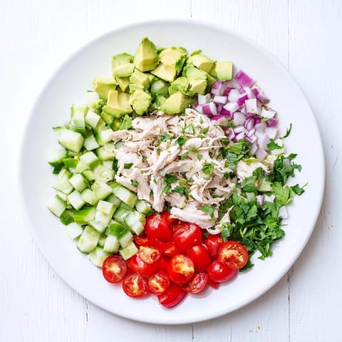 A close-up of creamy Avocado Chicken Salad with red onion and cherry tomatoes on a rustic plate.  