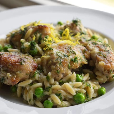 Vibrant Lemon Herb Chicken Orzo Skillet simmering in a pan, with tender chicken pieces, bright green peas, and fresh parsley garnish.