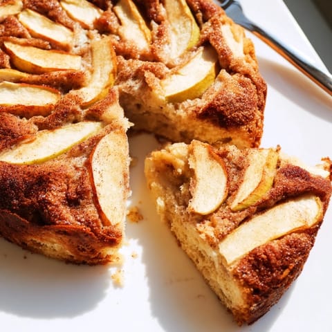 Warm Baked Apple Cake is served on a white plate, revealing a moist crumb with soft, spiced apples perfect for a comforting breakfast.