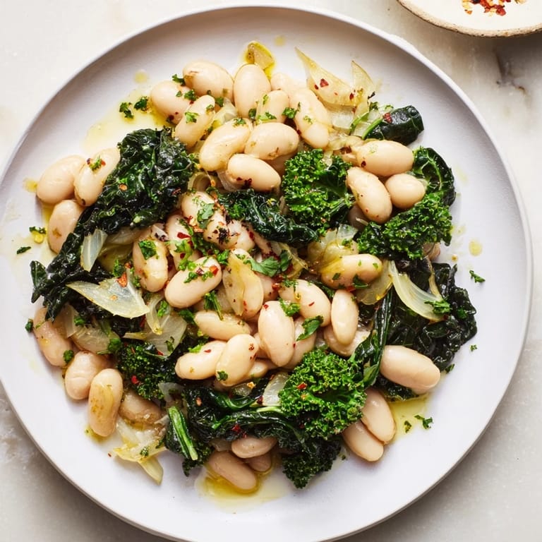 A rustic bowl of Garlicky Beans with Winter Greens, lemon is drizzled, ready for a comforting bite.