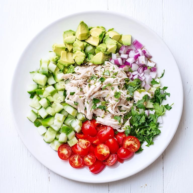 A close-up of creamy Avocado Chicken Salad with red onion and cherry tomatoes on a rustic plate.  