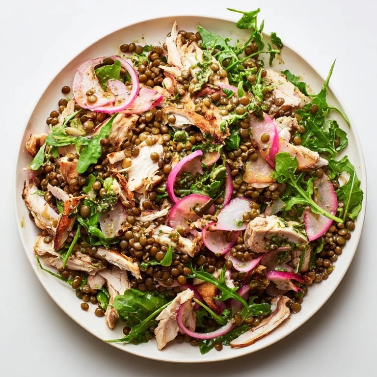 Fresh arugula and cherry tomatoes top a bowl of warm lentils and roasted chicken, drizzled with a zesty mustard dressing.