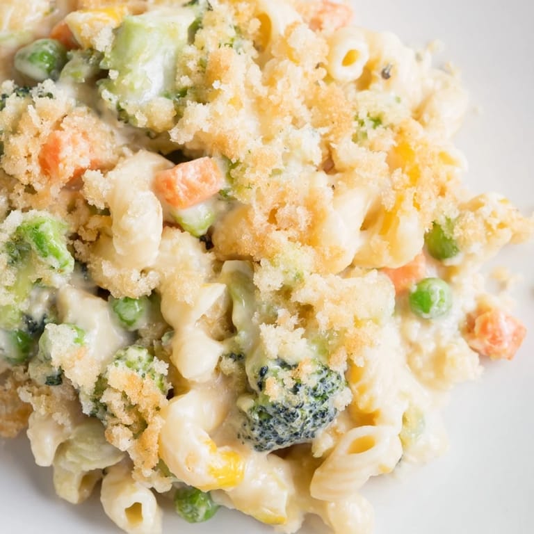 Serving suggestion for hearty Garden Veg Mac and Cheese, with a spoon lifting a cheesy portion revealing peas and carrots in a creamy sauce.