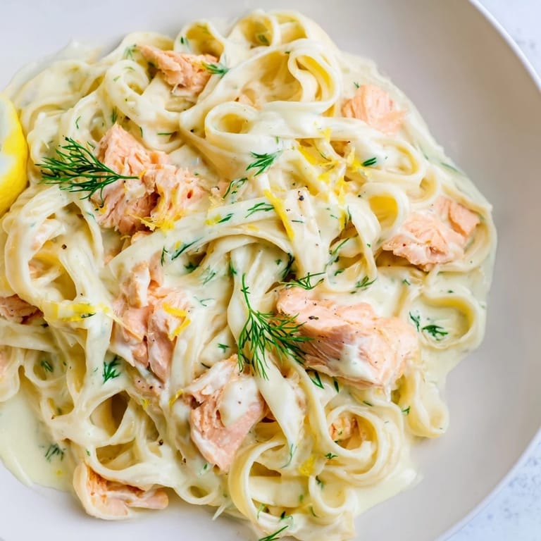 A close-up of creamy salmon pasta garnished with fresh parsley and lemon zest, steam rising from the skillet.