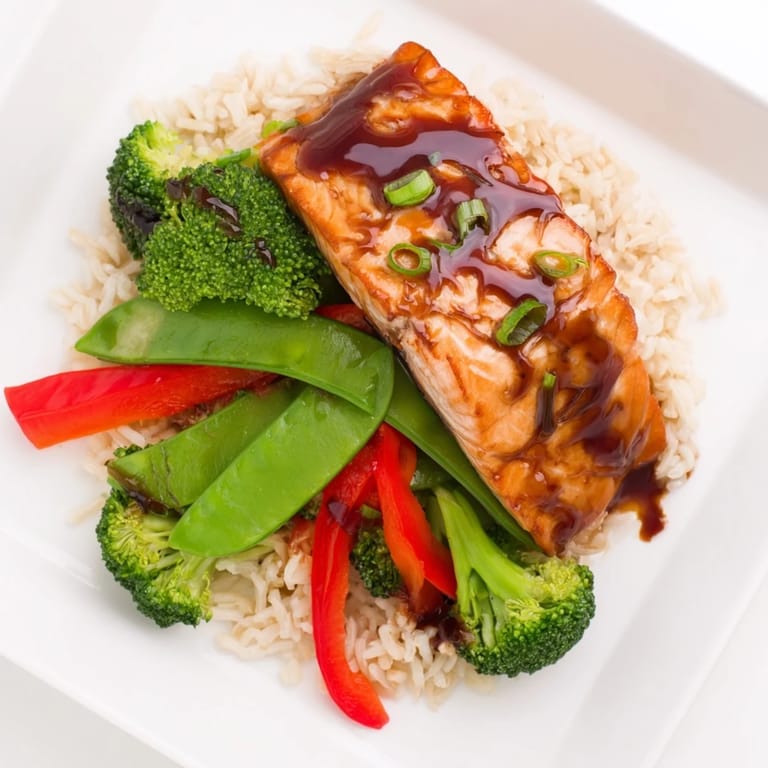 Glossy Maple Soy Glazed Salmon garnished with green onions and sesame seeds, next to crisp-tender Asian vegetables.