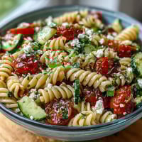 Lemon Vinaigrette Pasta Salad with Cucumbers and Cherry Tomatoes in a white bowl, garnished with parsley and feta cheese.
