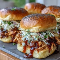 Juicy BBQ chicken sliders topped with tangy coleslaw on soft toasted buns, perfect for 4th of July parties.  